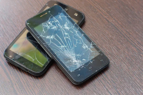 Dos teléfonos inteligentes negros rotos se encuentran el amigo en el amigo sobre un fondo de madera . — Foto de Stock