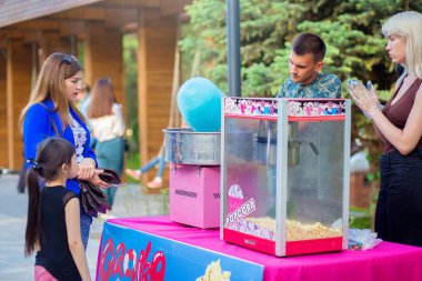 Volgograd, Rusya, 05.20.2019: Adam parktaki santrifüjde mavi pamuk şeker yapıyor, çocuklu anne tatlı alıyor