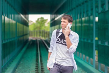 Bir tünelin arka planına karşı raylar üzerinde bir sırt çantası ile beyaz gömlekli genç adam ve telefonla aramalar