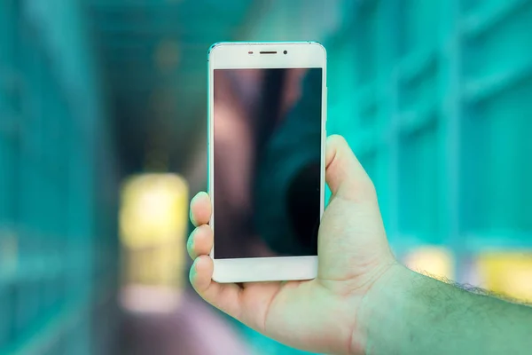 El gran teléfono inteligente blanco en una mano de cerca sobre el fondo de un túnel . — Foto de Stock