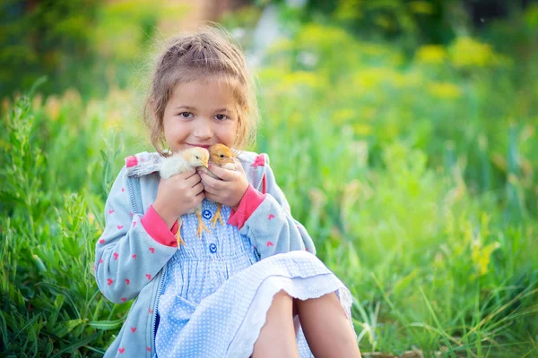 Het kleine meisje zit in een gras in het dorp en houdt in de hand van twee kippen — Stockfoto