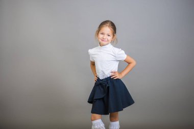 Kız bir okul üniforması içinde birinci sınıf - bir etek ve beyaz bir bluz gri bir arka plan üzerinde pozlar