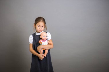 Birinci sınıf öğrencisi kız bir bebeği kucaklar ve okula gitmek için gerekli olduğunu çok uzun.