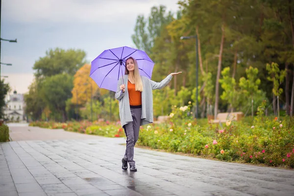Молодая красивая девушка ходит осенью под зонтиком и проверяет рукой, идет ли дождь — стоковое фото
