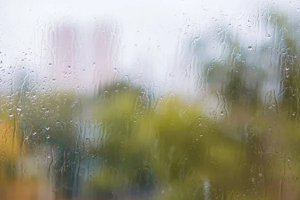 Gotas de lluvia fluyen por el vidrio contra el telón de fondo de un patio de otoño — Foto de Stock