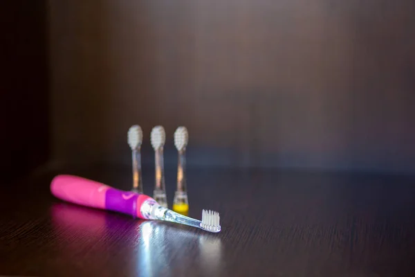 Uno spazzolino da denti elettrico rosa retroilluminato alimentato a batteria con tre ugelli intercambiabili si trova su uno scaffale — Foto Stock