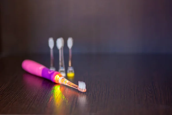 Pille çalışan, pembe renkli, elektrikli pembe bir diş fırçası ile rafta üç tane değiştirilebilir başlık var.