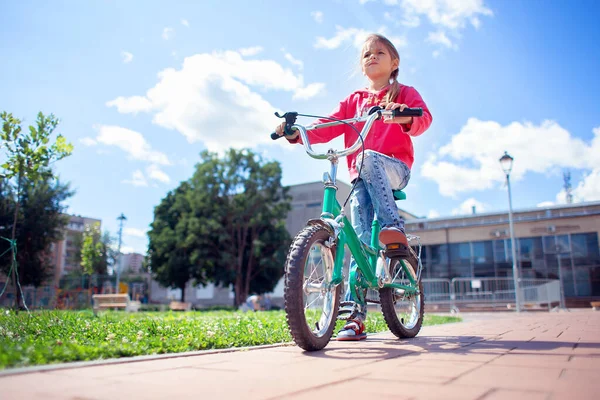 A girl in ripped jeans rides a bicycle in the park. Bottom view