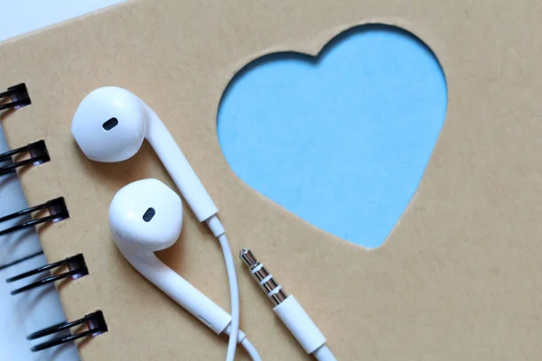 White earphones on a notebook with blue heart