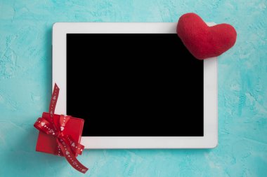 Romantik bir hediye ve peluş kalp ile mavi bir yüzey üzerinde beyaz tablet. Mutlu Sevgililer Günü kartı.