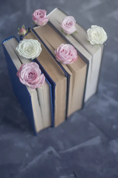 Pile of the old books with pink roses on the concrete surface. Vintage background
