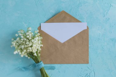 Lily vadi buketi ve mavi yüzeyüzerinde zanaat kağıt zarf. Üst görünüm bahar çiçek kartı