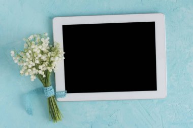 Lily mavi yüzeyde beyaz tablet bilgisayar ile vadi buketi. Üst görünüm bahar çiçek kartı