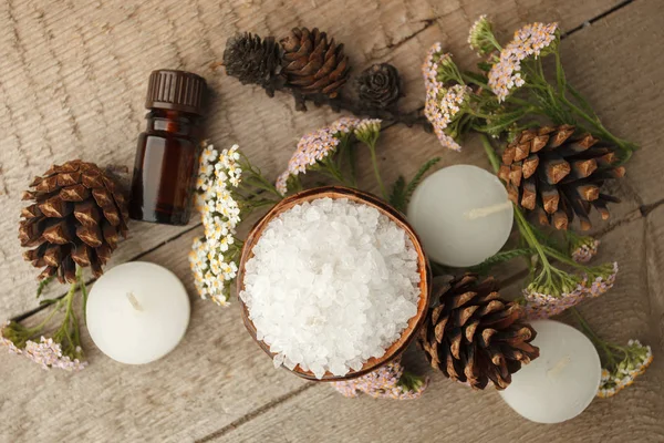Spa and wellness setting with sea salt, oil essence, cones and candle on wooden background. Fall autumn wellness concept, Relax and treatment therapy. Close up