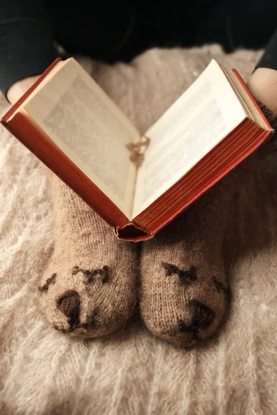 Soft photo of woman legs in cute funny bear brown socks on the bed with old book, monochrome concept, time for read, fall and winter season