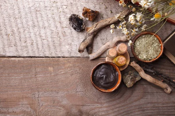 Preparing cosmetic black mud mask in ceramic bowl on vintage wooden  background. Top view of facial clay emulsion on table with spa products. Natural cosmetics for home or salon treatment