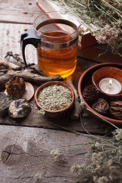 Healthy tea in glass teapot, dry herbs, plants and stones on wooden table. Homeopathy, alternative, occult ritual and herbal medicine concept, monochrome, vertical