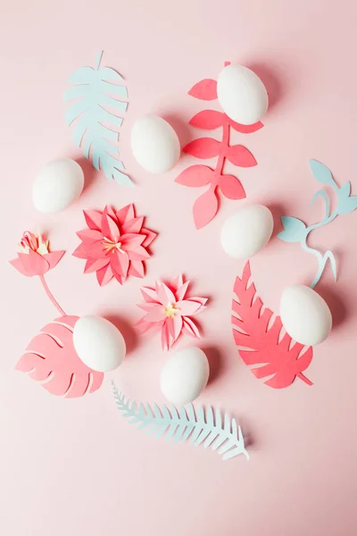 modern easter decor idea - white eggs and origami paper craft flowers and plans on pink pastel background