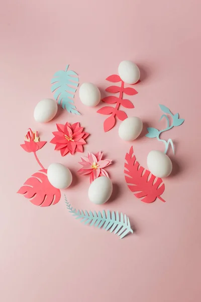 modern easter decor idea - white eggs and origami paper craft flowers and plans on pink pastel background