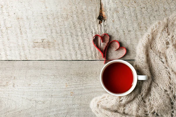Cup of tea with heart shape and warm woolen sweater plaid scarf on vintage wooden table, minimal concept of valentine mother day morning breakfast