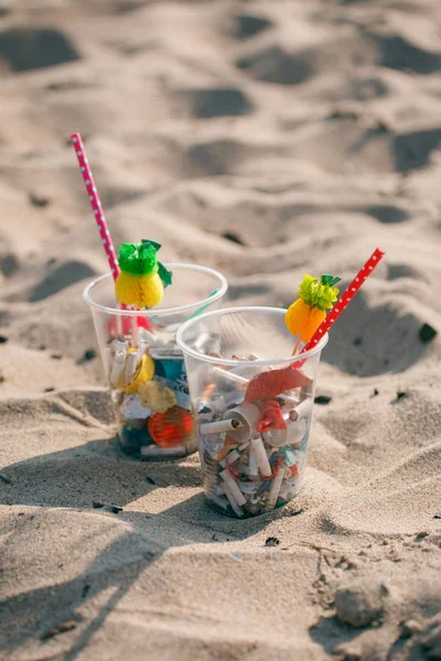 Cocktail with garbage and tropical decor on clean beach. Plastic