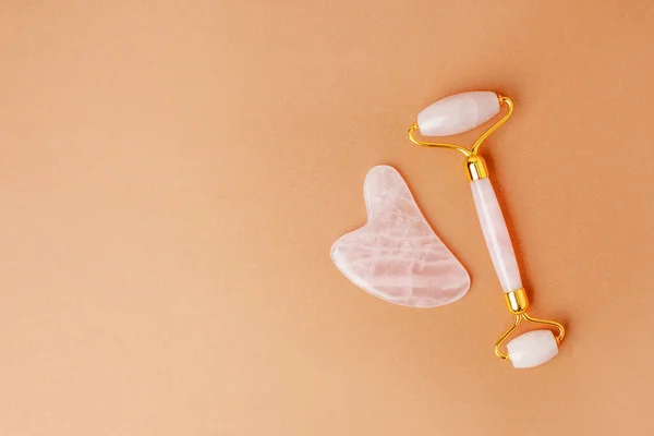 Pink quartz jade roller and gua sha tool stone on modern beige  background. Trendy beauty tool. Minimal composition, copy space, beauty blogger life style card