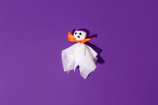 Decoration for Halloween party - ghost from paper napkin and orange bow on traditional bright violet purple background, creative concept of night party, trendy hard shadow, flyer for promotion