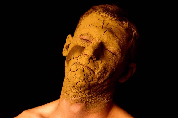 Face closeup portrait on black background. Dried clay on the face, cracked skin. Display of empty on the face.