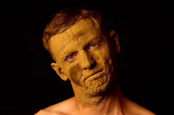 Face closeup portrait on black background. Dried clay on the face, cracked skin. Display of empty on the face.