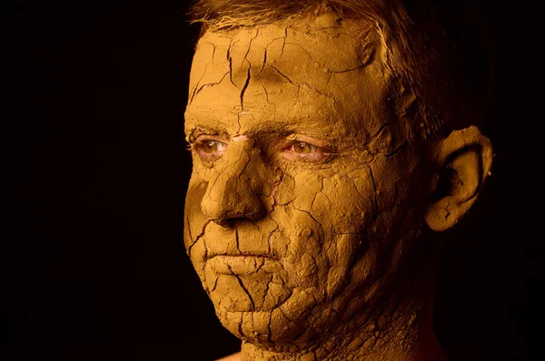 Face closeup portrait on black background. Dried clay on the face, cracked skin. Display of empty on the face.