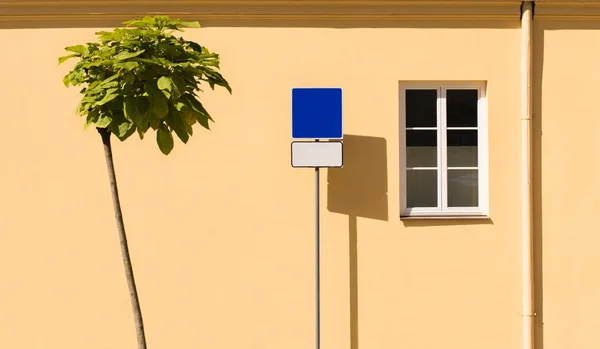 Against the background of a yellow wall, a tree and a road sign copy space