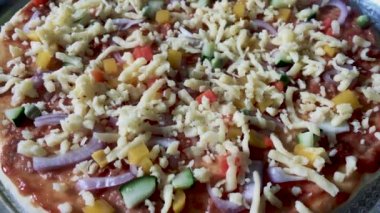 Pizzanın üstüne çeşitli malzemelerle ev yapımı çiğ pizza. Fırında pişirmeden önce peynir ekiyorum..