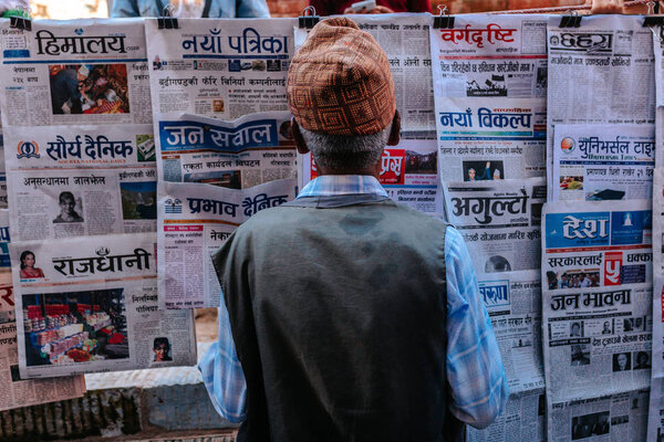 Задний вид человека в подлинной шляпе, смотрящего на непальские газеты
