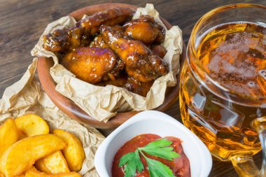 Susam ile güzel kokulu ve keskin soslu tavuk kanatları. Bir bardak taze soğuk bira ve taze domates ve otlar rustik domates soslu patates kızartması...
