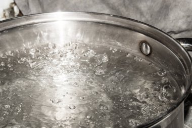 Paslanmaz çelik tencere üzerinde bir gaz sobası ve su kaynar.