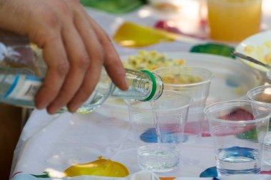 Votka plastik gözlük içine dökülür. Bir adamın elinde bir şişe.