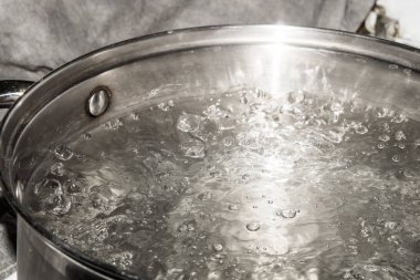 Paslanmaz çelik tencere üzerinde bir gaz sobası ve su kaynar.