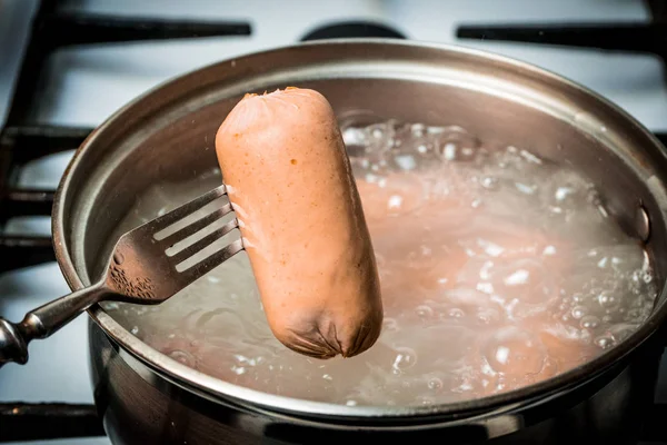 Готувати ковбаски на сковороді з нержавіючої сталі на газовій плиті . — стокове фото