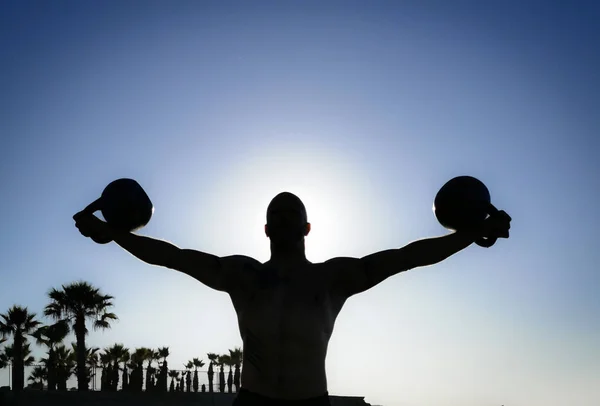 A Silhouette of a Male Kettlebell Lifter on the Beach Performing the Iron Cross