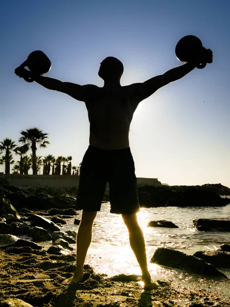 A Silhouette of a Male Kettlebell Lifter on the Beach Performing the Iron Cross