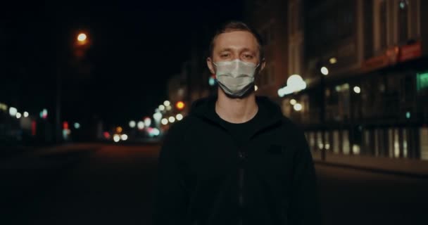 Мужчина в маске смотрит в камеру на городской улице ночью. Ковид-19 вируса Короны . — стоковое видео