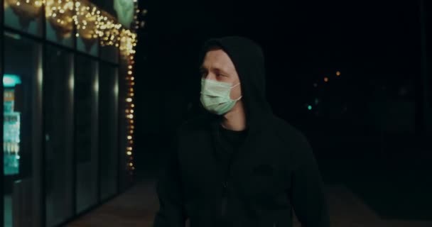 Человек в маске с капюшоном ходить ночью улице среди рынка короны вирус ковид-19 4K . — стоковое видео