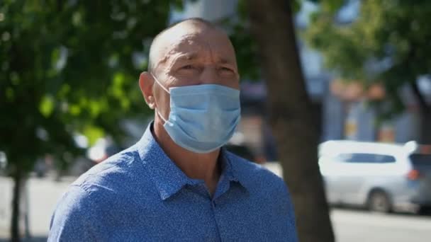Old tourist without Covid-19 looks at camera in empty park wearing medical mask. — Stock Video