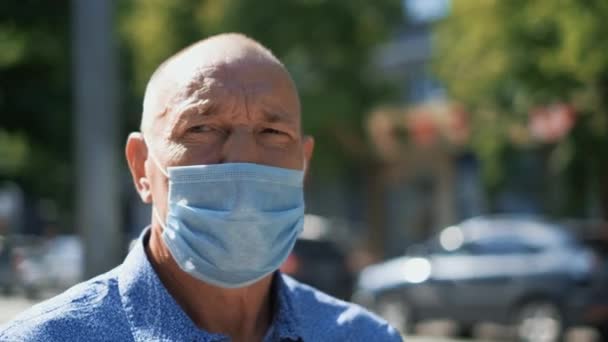 Un aîné regardant une caméra dans un parc porte un masque médical. Coronavirus. Covid-19. — Video