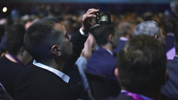 La gente hace foro de negocios de audiencia llena de teléfono fotográfico. Oyente de auditorio hombre — Vídeos de Stock