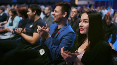 Gülümseyen iş kadını konuşmacıyı alkışlıyor. Seminer büyük izleyicileri mutlu eder.