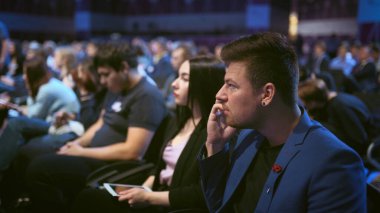 İş adamı kalabalık dinleyicilerle konuşuyor. İnsanlar eşle cep telefonu konuşur