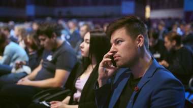 İş adamı kalabalık dinleyicilerle konuşuyor. İnsanlar eşle cep telefonu konuşur