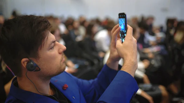 Persona che prende il telefono della fotografia. Uomo d'affari ascoltare lezione in pubblico folla. — Foto Stock