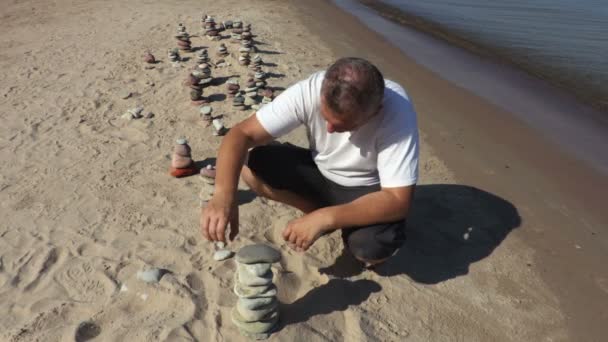 Homem Constrói Pirâmide Pedra Equilibrada Praia — Vídeo de Stock